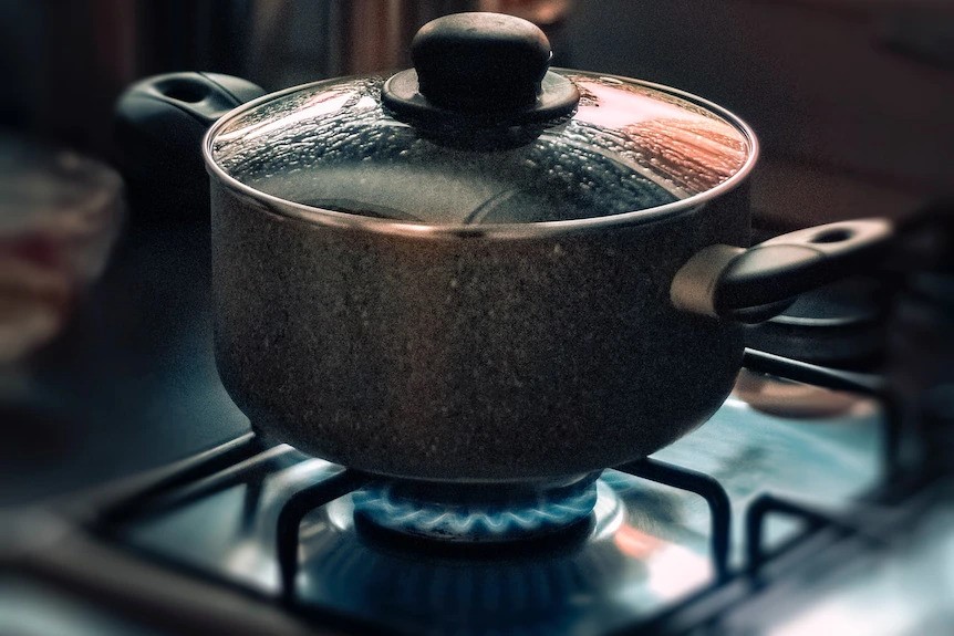 A large pot with a lid and handles boiling on a gas stove