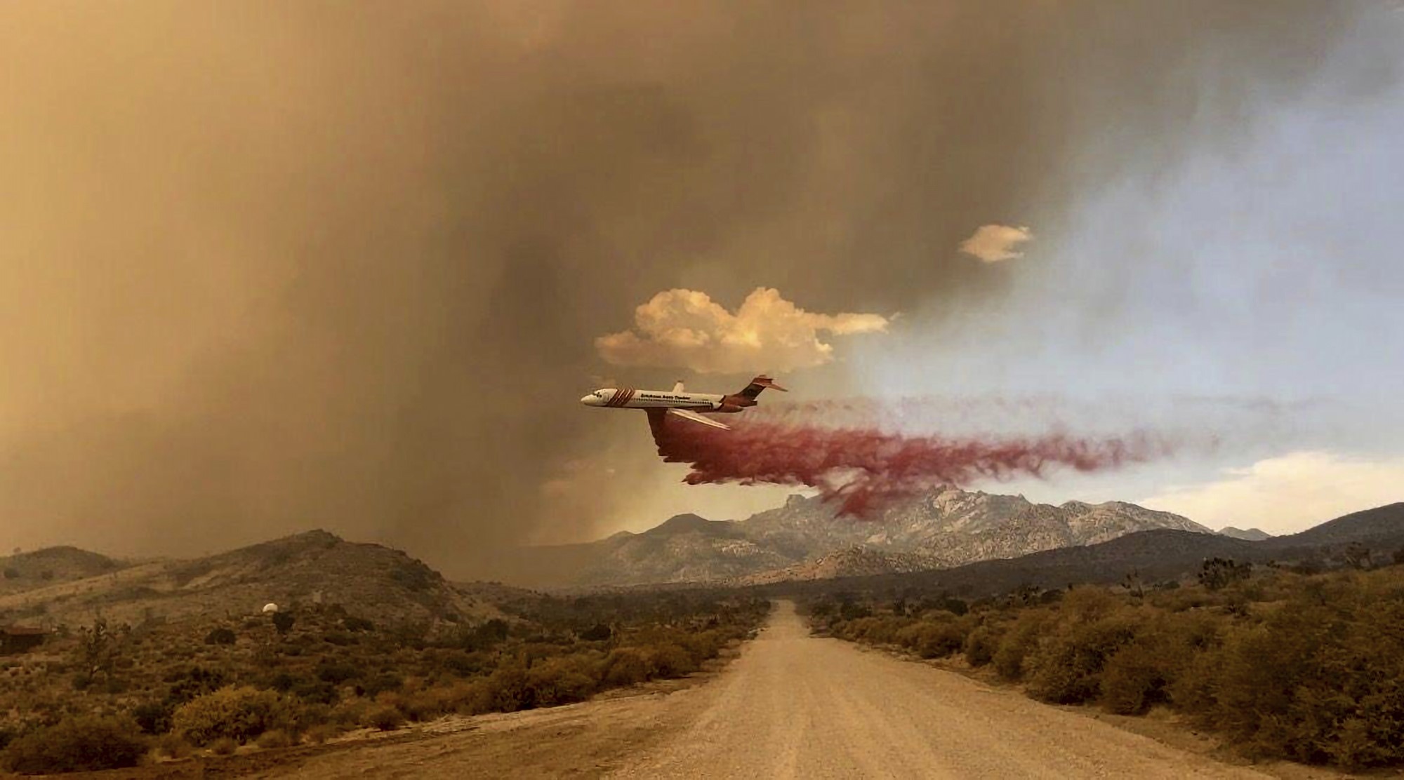 A plane dropping red smoke over a dirt road. 